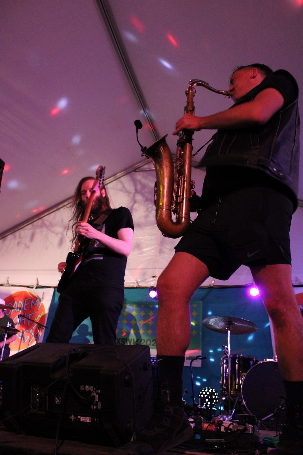 A low-angle view of a saxophonist leaning back, with another performer behind.