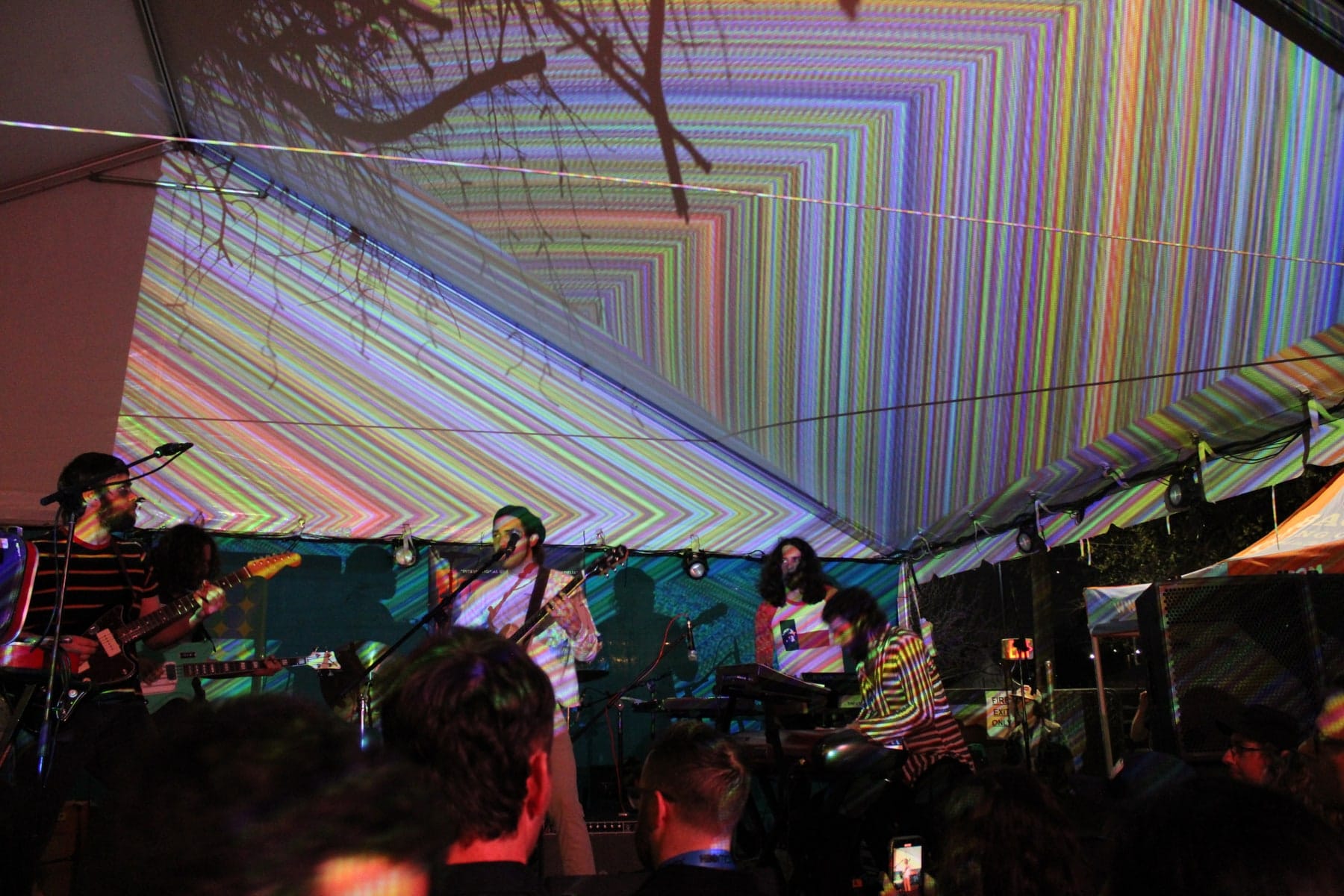 An audience watches a stage beneath patterned projections.