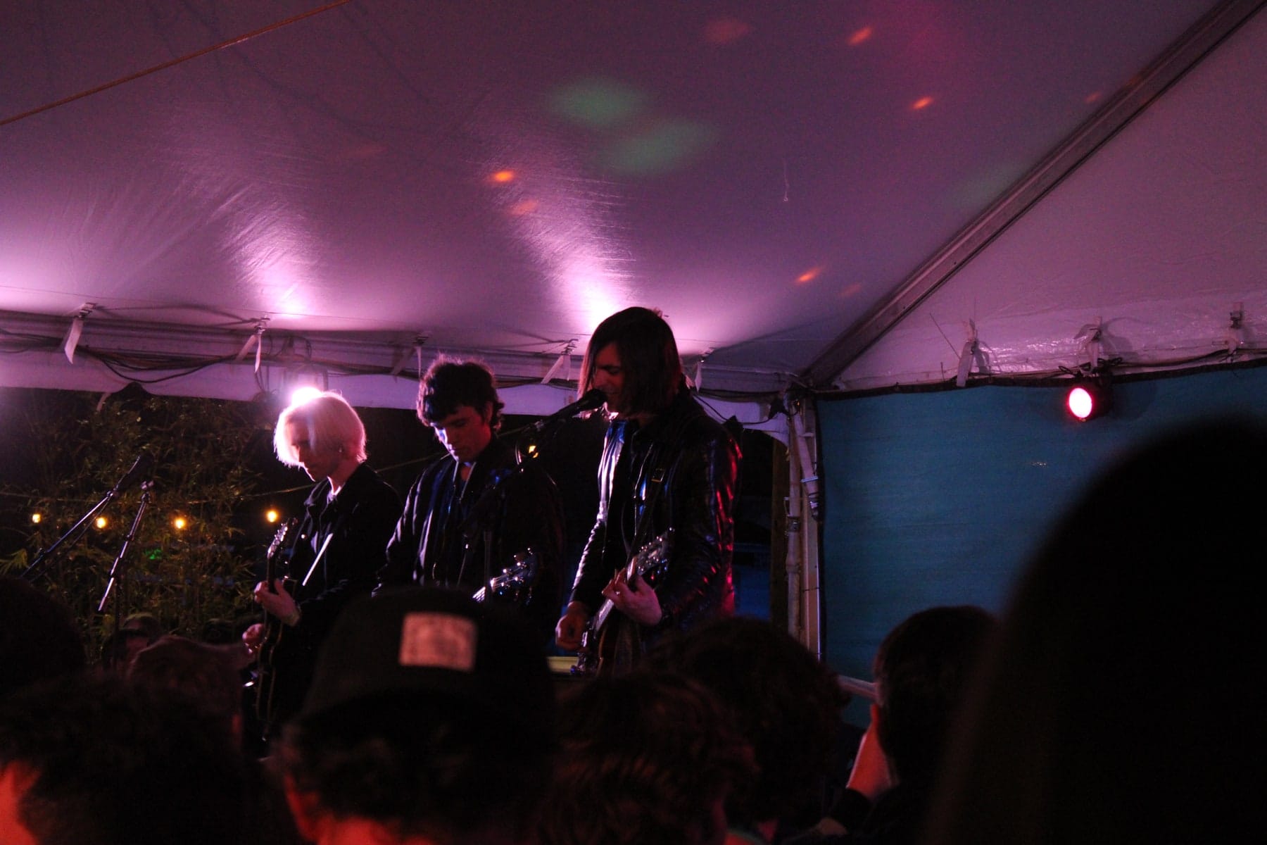 Three performers outlined by colored light behind audience silhouettes.