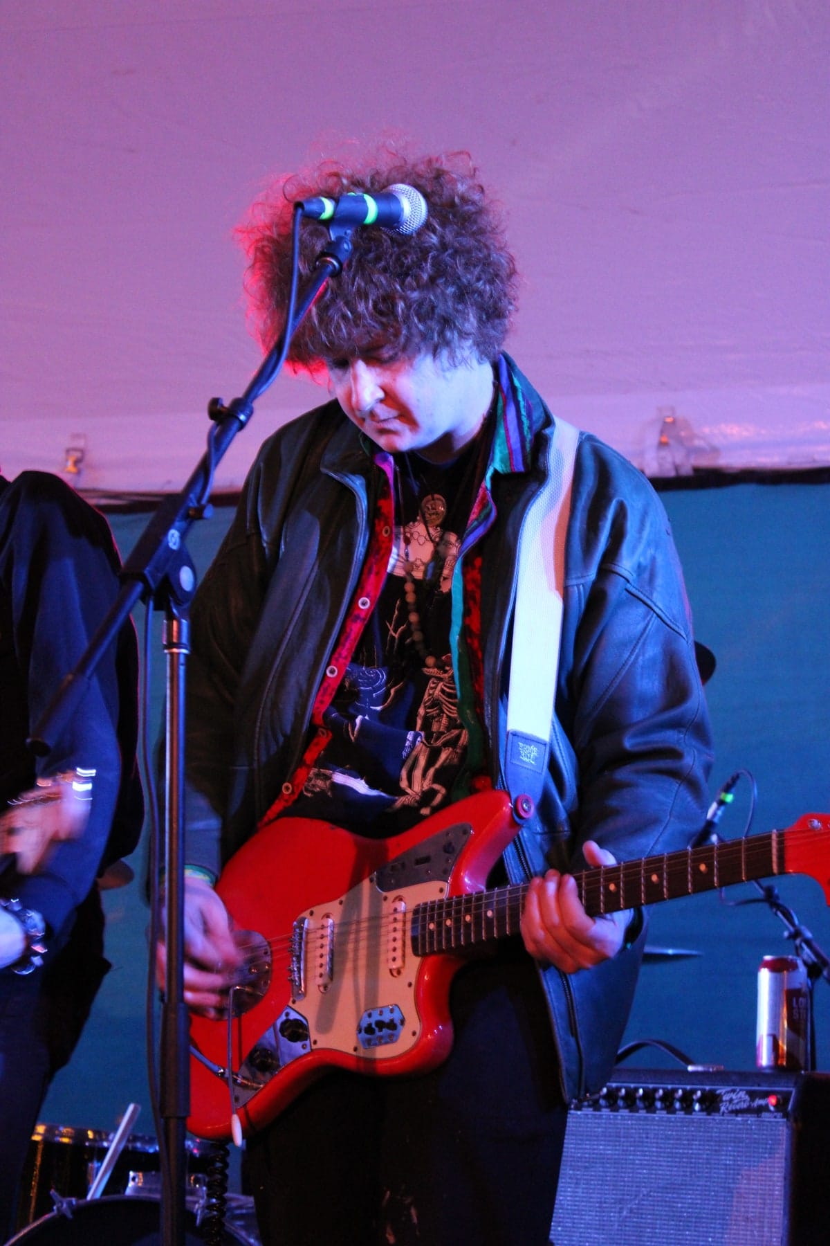A guitarist looks down at a red guitar under blue and purple lighting.